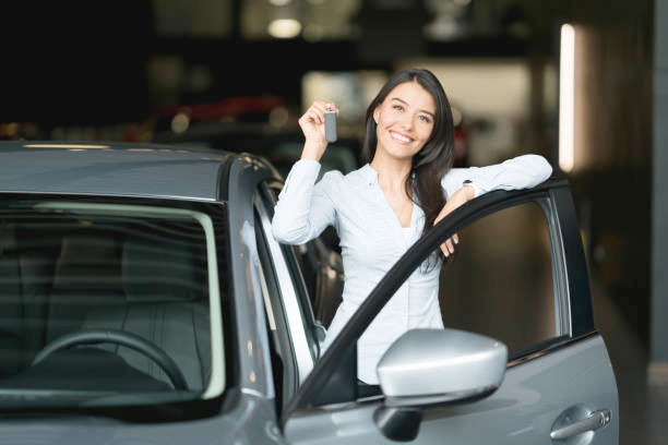 A smiling woman holding car keys in front of a new sedan
